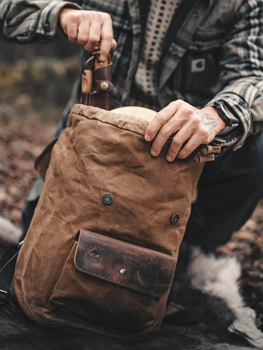 Miljöbild föreställande man i skogen som plockar ut någonting ur en ryggsäck av modellen Ayers Rocki beige kanvas med detaljer i läder från varumärket Scippis